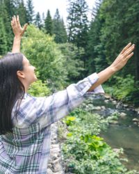 Happy young woman in a forest in a mountainous area enjoys nature near the river.